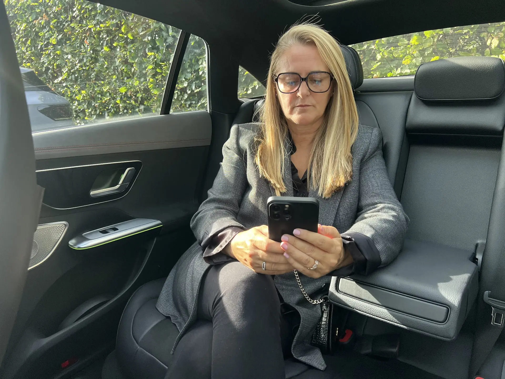 Passagère en veste de tailleur assise à l'arrière du taxi Mercedes EQE, consultant son téléphone