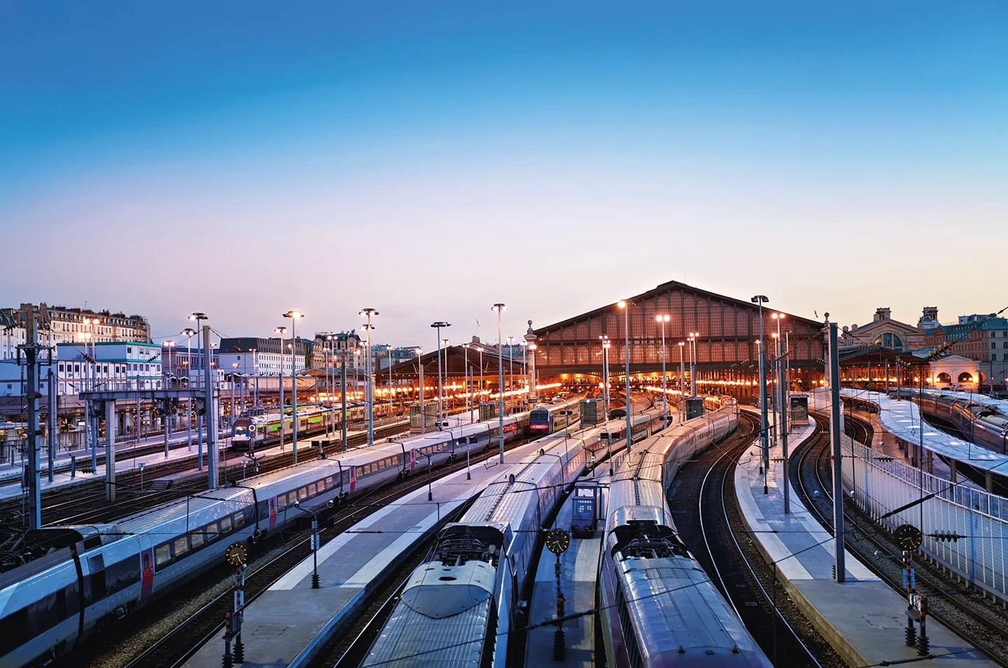 Quais et rames à grande vitesse d'une gare parisienne au crépuscule